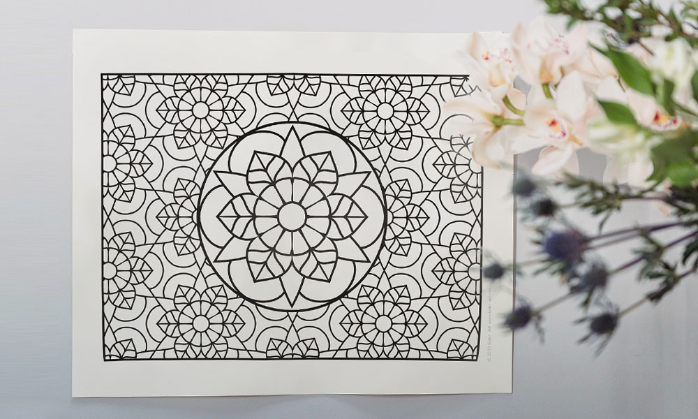 Mandala pattern coloring page. There are flowers on the right side of the picture slightly on top of the coloring page.