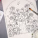 Coloring page, watercolor supplies, and flowers on a table. The coloring page features an elf surrounded by peonies.